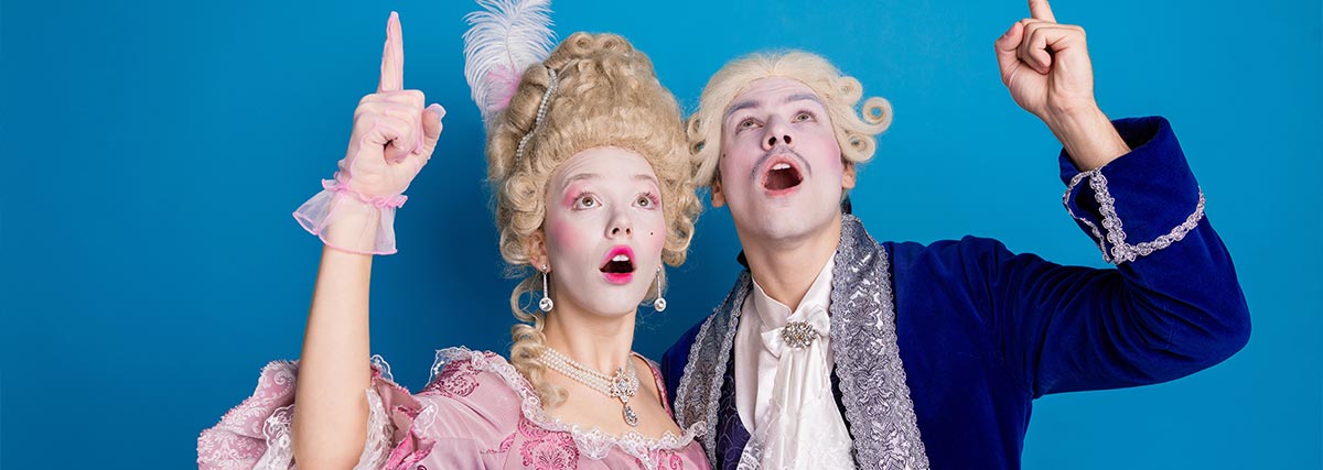 A man and woman in luxurious baroque attire gesture dramatically on a bright blue backdrop
