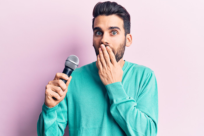 Bearded man holding a microphone and covering his mouth afraid of mistake