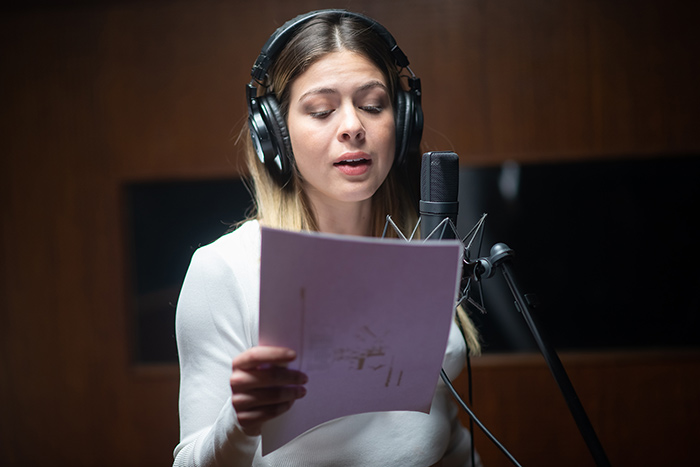 Beautiful woman singing holding sheet music in studio