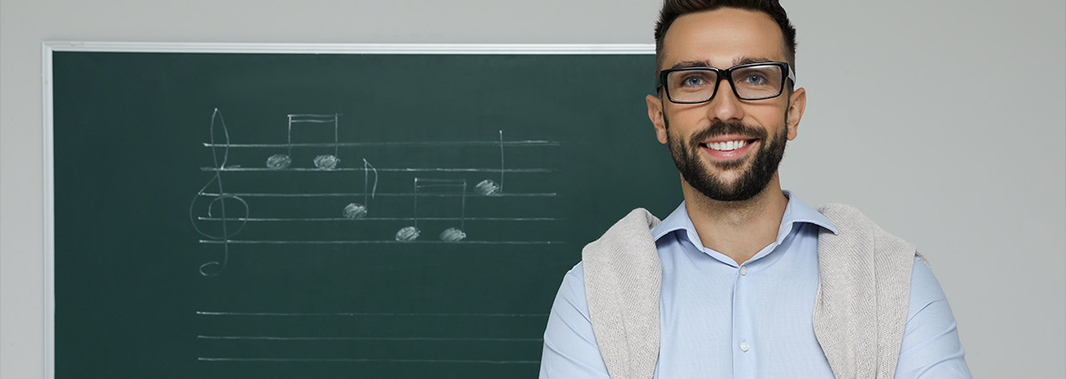 Male music teacher smiling with a board showing written music notes in the background