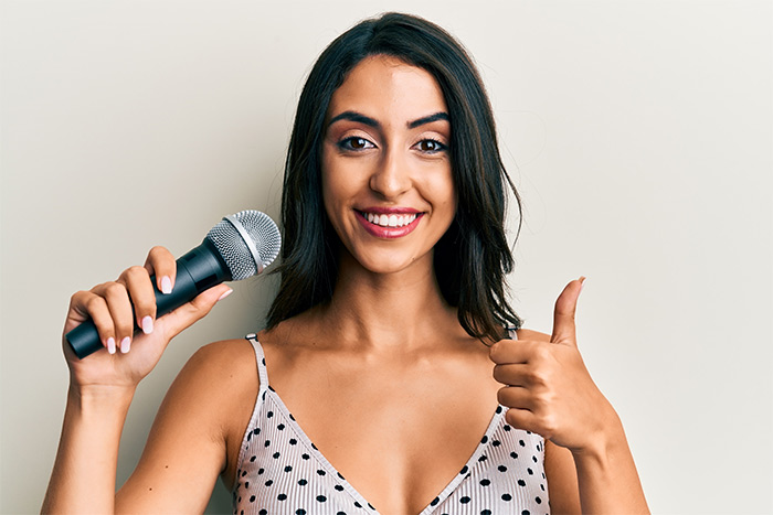 Woman smiling holding a microphone and doing an OK sign feat